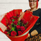 a lady holding a bouquet of 12 red roses in floral wrap. 