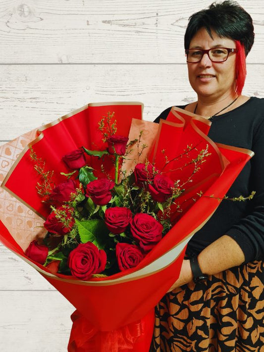 a lady holding a bouquet of 12 red roses in floral wrap. 