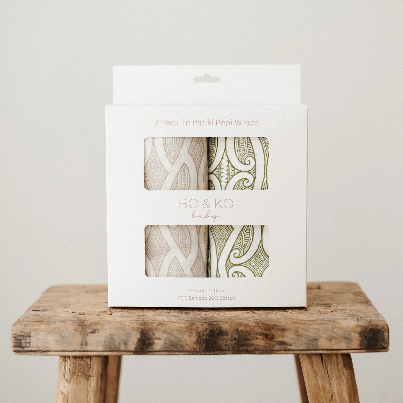 Pack of BO & KO baby wraps on a wooden stool with a plain background