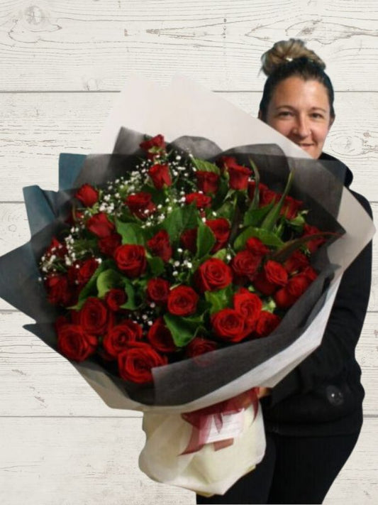 50 roses with greenery giftwrapped held by a person