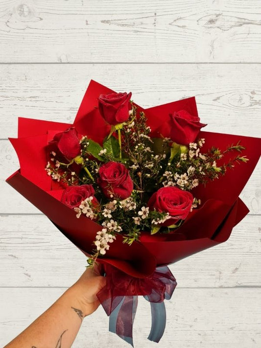 6 red roses with white floral greenery giftwrapped and held