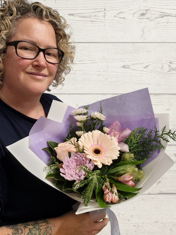 Person holding a bouquet of pink and white flowers on a white wooden surface