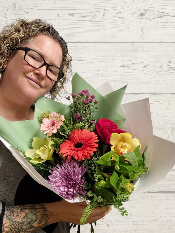 A person holding a large bouquet of colorful flowers with green wrapping paper.