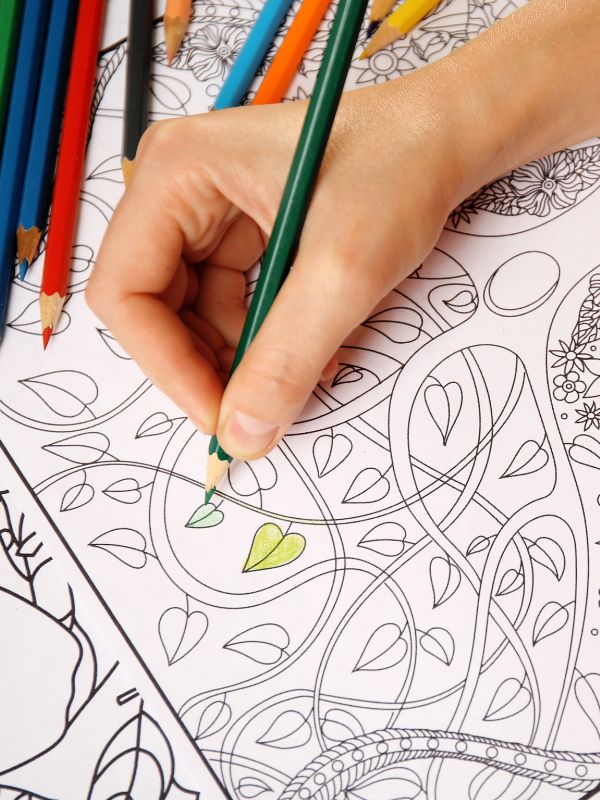 coloring-in book with coloured pencils and a hand, with vines and leaves