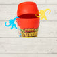 red barrel of monkeys with 2 monkeys hanging on the open lid on a wooden background