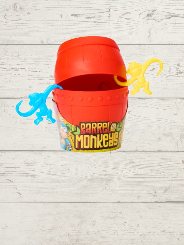 red barrel of monkeys with 2 monkeys hanging on the open lid on a wooden background