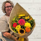 bright bouquet of flowers in a harakeke flax wrap with yellow bow