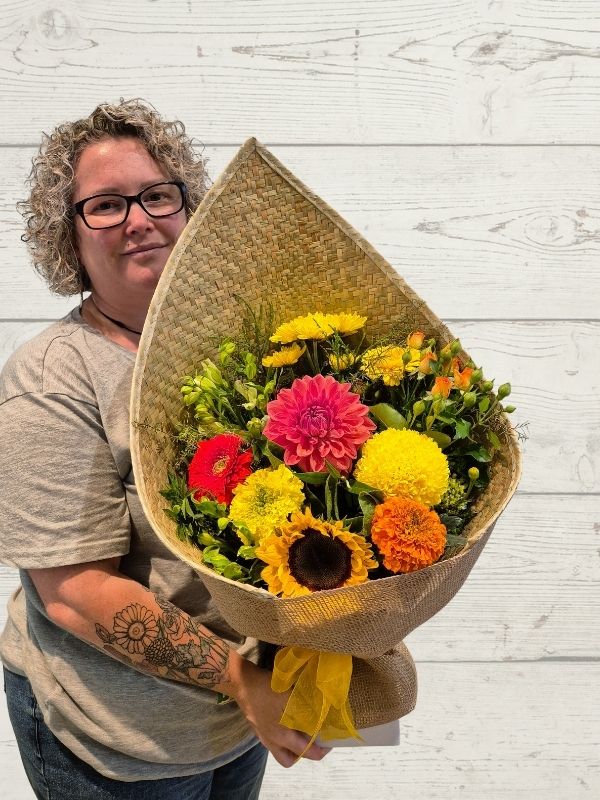 bright bouquet of flowers in a harakeke flax wrap with yellow bow