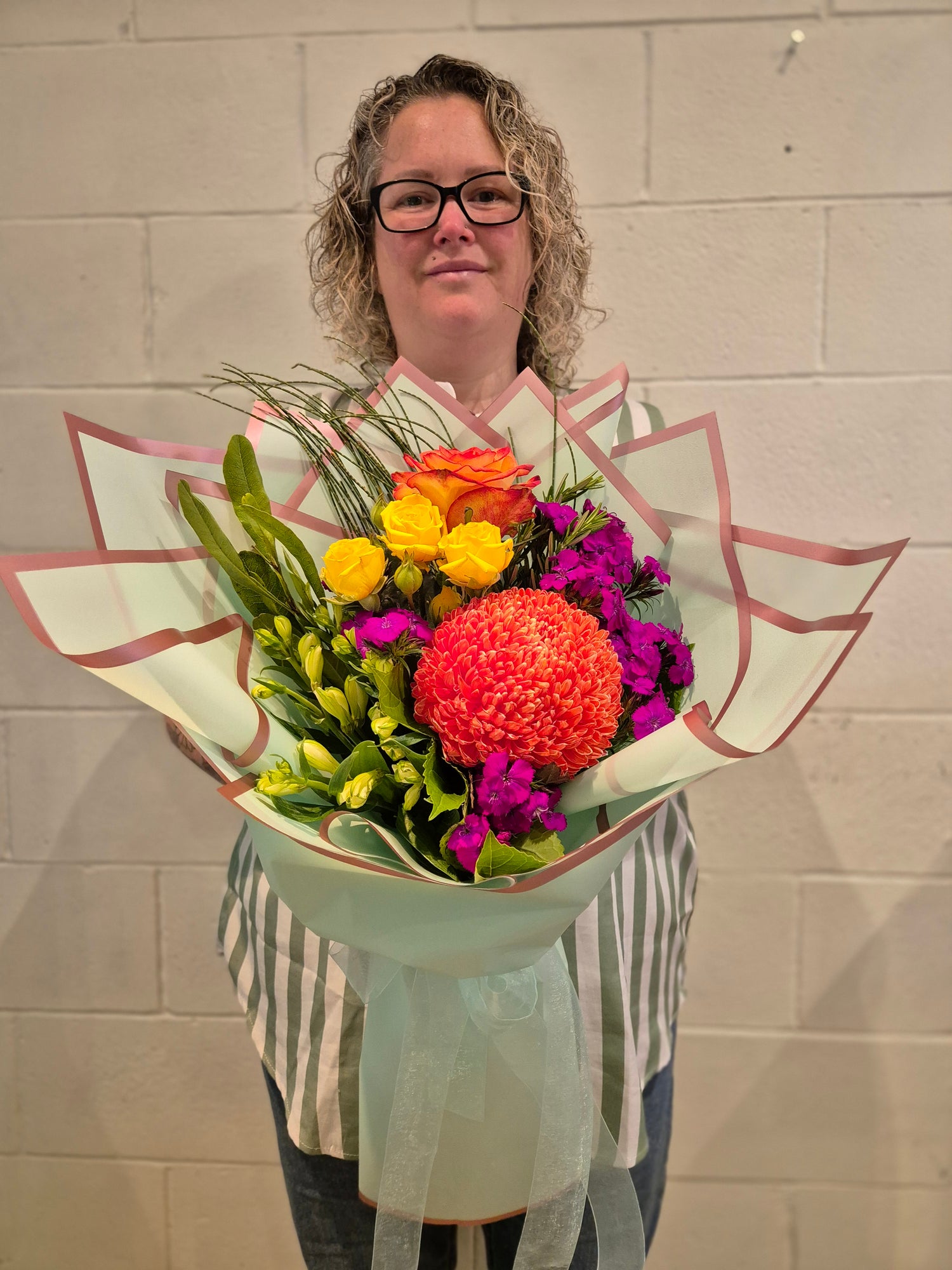 bouquet of bright flowers held by a person on a white brick background. 