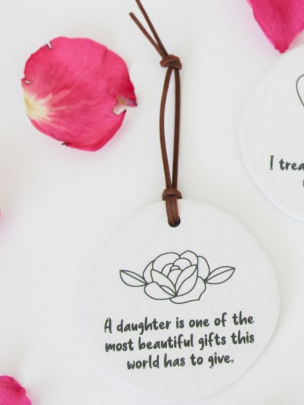 A white ceramic plaque with an embossed floral design and a rope for hanging, featuring a quote about a daughter.