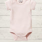 A pink short-sleeve rib bodysuit for babies, with a round neckline and side snap opening, displayed on a wooden background.