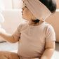 A baby wearing a pink organic cotton modal darcy rib tee bodysuit with a bow on the hood.