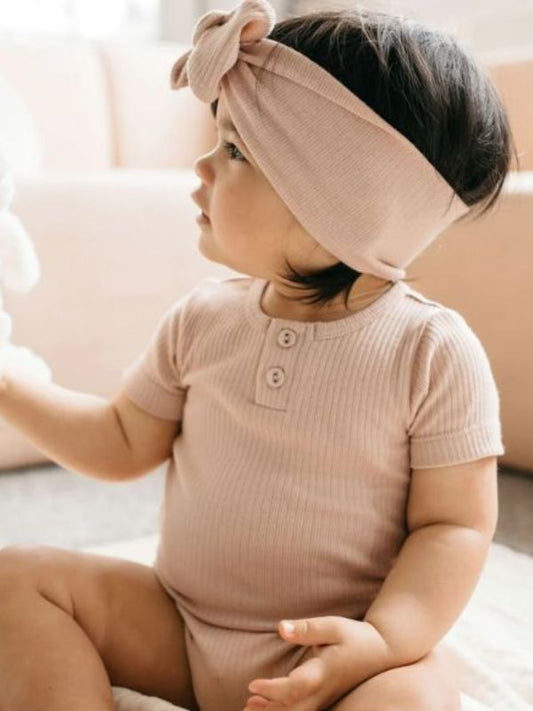 A baby wearing a pink organic cotton modal darcy rib tee bodysuit with a bow on the hood.