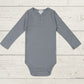 A long sleeve blue bodysuit for babies, presented on a wooden background.