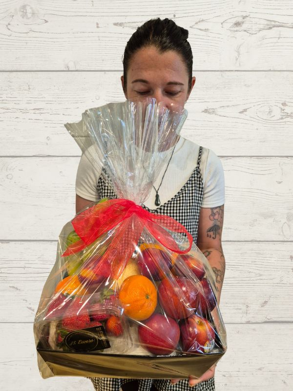 A tray of fruit giftwrapped held by a person on a white wooden background