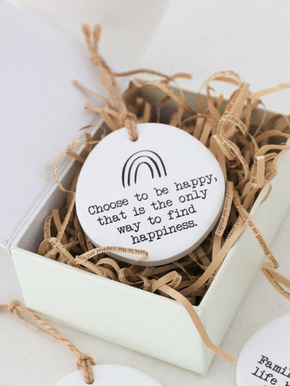 A white ceramic keepsake with a embossed rainbow and the quote 'Choose to be happy, that is the only way to find happiness.' It has a rope for hanging and is presented in a box with a family tree design.