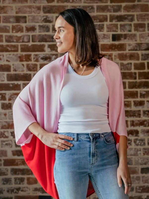 A person standing in front of a brick wall, wearing a red cardigan over a white top and blue jeans.