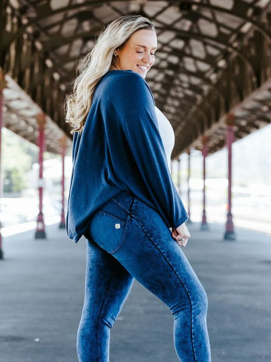 A woman is wearing a navy cardigan with kimono style sleeves over a white top, paired with blue jeans.
