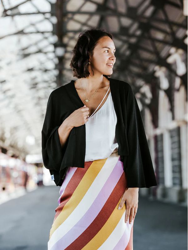 A woman is wearing a black cardigan with kimono style sleeves over a white top, paired with a colourful skirt.