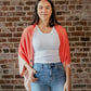A person standing in front of a brick wall, wearing a red cardigan over a white top and blue jeans.