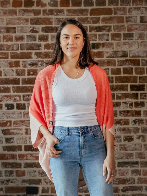 A person standing in front of a brick wall, wearing a red cardigan over a white top and blue jeans.