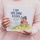 A person holding a children's book titled 'I Got You Some Kisses', featuring illustrations of a bear and a rabbit on the cover.