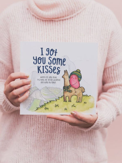A person holding a children's book titled 'I Got You Some Kisses', featuring illustrations of a bear and a rabbit on the cover.