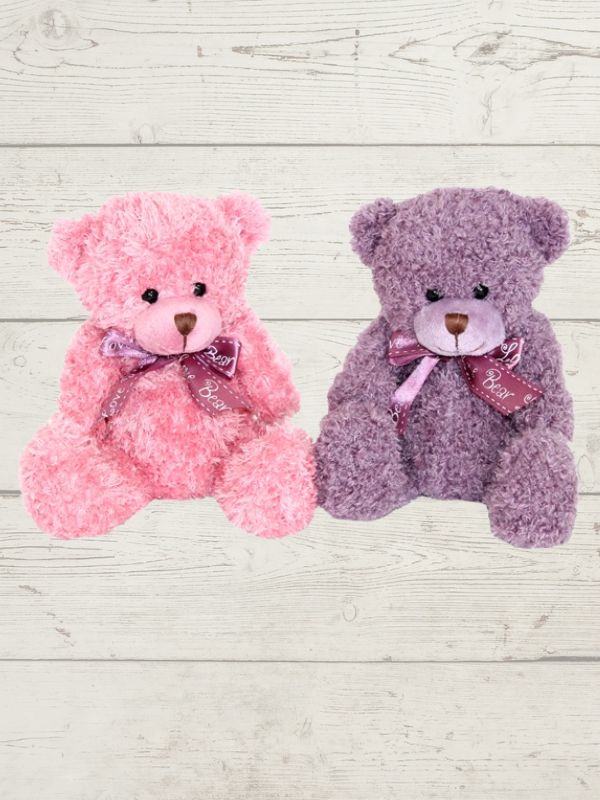 Two soft toy bears, one in pink and one in purple, each with a bow ribbon around their neck, placed on a wooden surface.