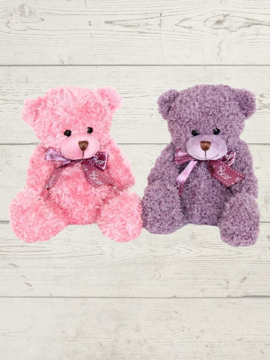 Two soft toy bears, one in pink and one in purple, each with a bow ribbon around their neck, placed on a wooden surface.