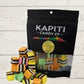Colorful licorice pieces in front of a black 'Kapiti Candy Co' bag on a light wooden surface.