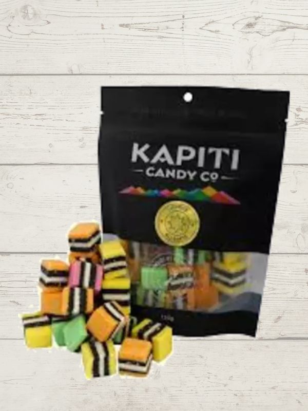 Colorful licorice pieces in front of a black 'Kapiti Candy Co' bag on a light wooden surface.