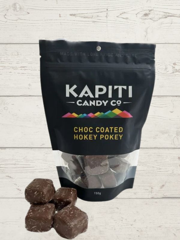 A black packaging bag with the label 'KAPITI CANDY CO CHOCOLATE-COATED HOKEY POKEY' along with a clear window showing the chocolate-coated hokey pokey candies inside.
