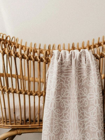 Woven basket with a white patterned cloth draped over it against a neutral background