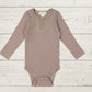 A long sleeve bodysuit for babies, in a beige color, presented against a wooden background.