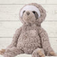A plush toy resembling a sloth with brown and white fur, featuring embroidered eyes and a soft texture.