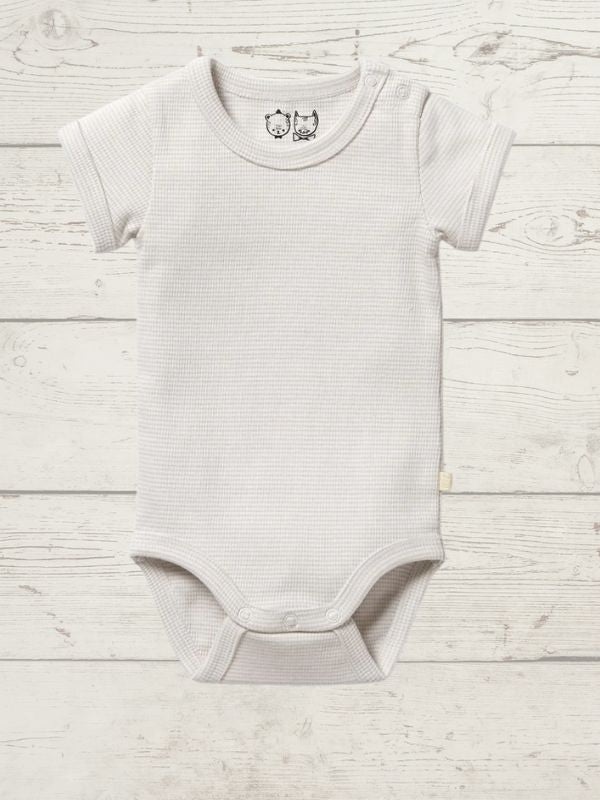 A beige short-sleeve rib bodysuit for babies, with a round neckline and side snap opening, displayed on a wooden background.