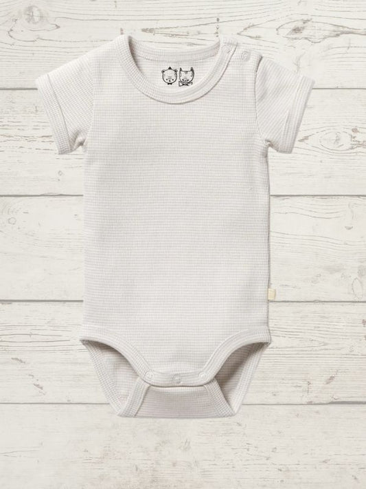 A beige short-sleeve rib bodysuit for babies, with a round neckline and side snap opening, displayed on a wooden background.