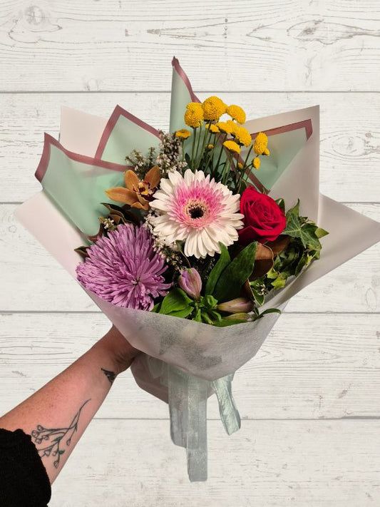 Bouquet of rainbow coloured flowers held by a person on a light wooden surface