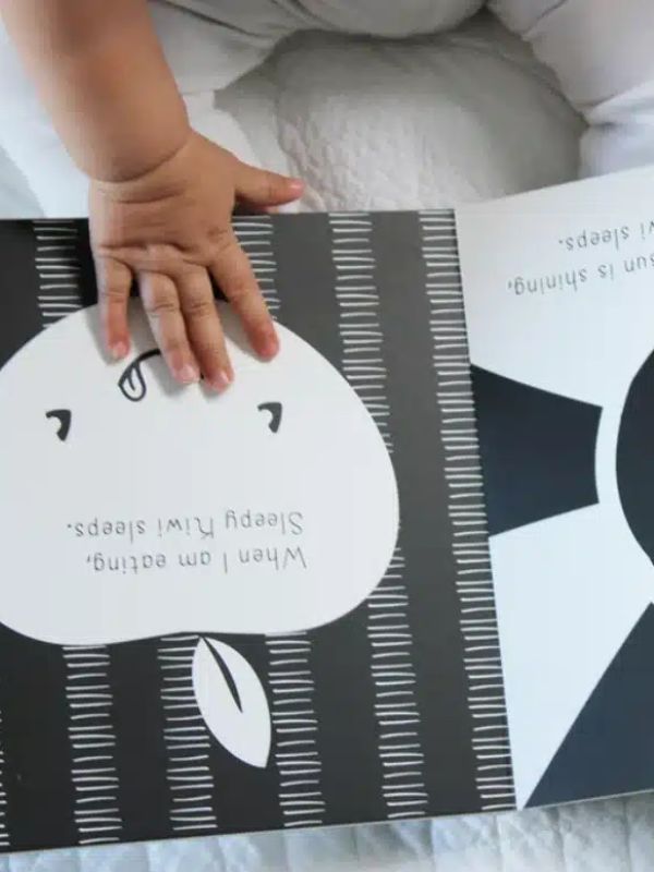 hard cover book with an apple on the page being held open by a little hand, black and white book on a blue blanket
