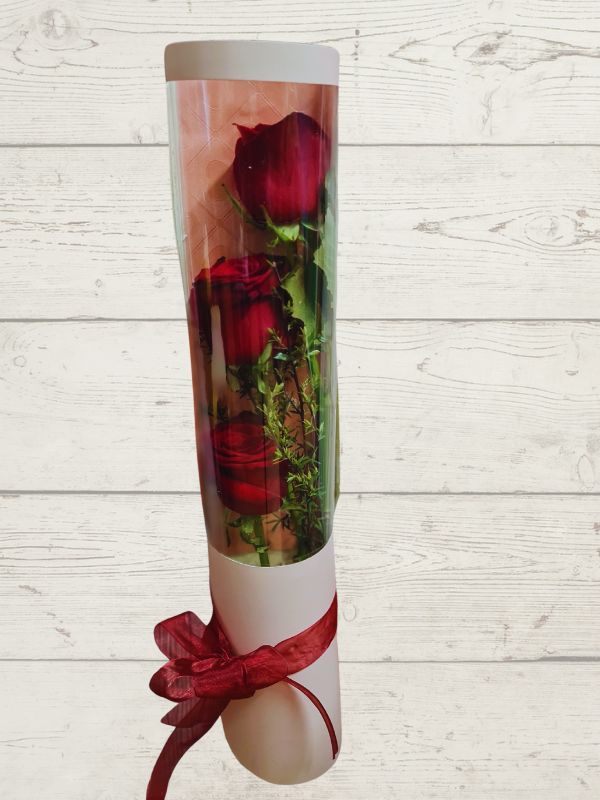 A cylinder gift wrap containing three red roses, tied with a red ribbon, presented against a wooden background.
