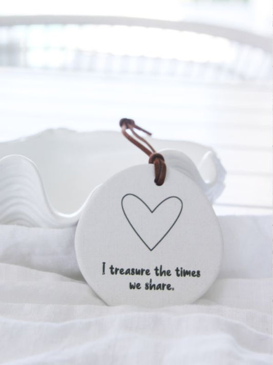 A white ceramic plaque with an embossed heart and the text 'I treasure the times we share', displayed on a white surface with a rope for hanging.