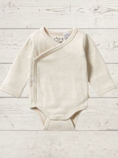 A beige long sleeve rib kimono bodysuit for babies, with a cross-over neckline and snap opening, displayed on a wooden background.