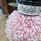 a black pottle with a white label on it with the words Lip Balm, on a pink chrysanthemum on a wooden surface 