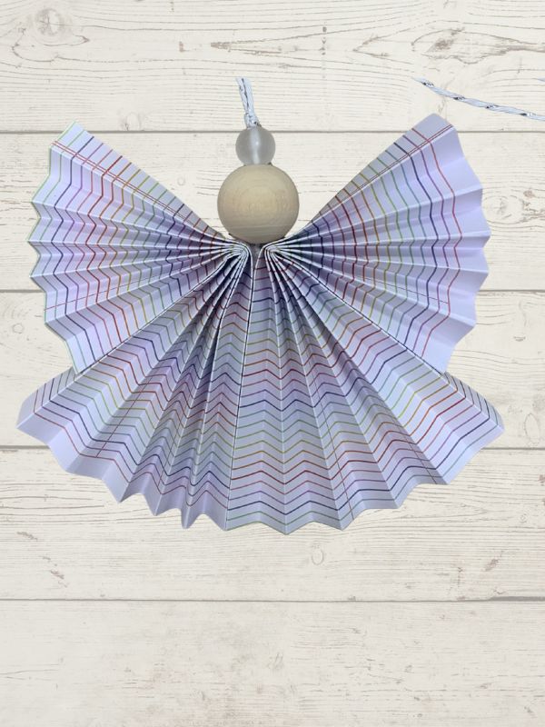 Decorative angel ornament with iridescent wings and a gray bead on a light wooden surface