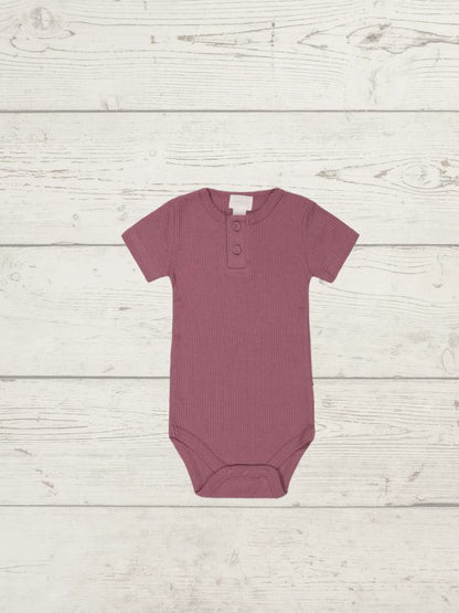 Mauve baby onesie on a light wooden surface