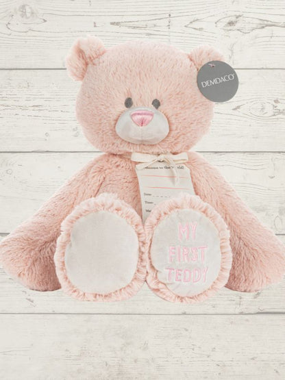 Pink teddy bear with 'My First Teddy' text on a wooden surface