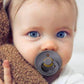 A baby holding a BIBS pacifier with an anatomical nipple design.