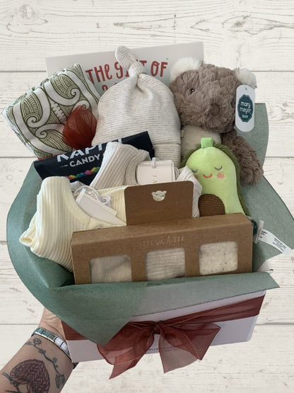 Gift basket with baby items including socks, a hat, and a plush toy on a light wooden surface.