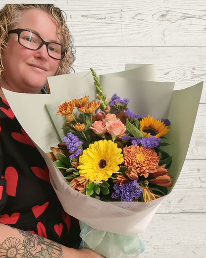 Person holding a bouquet of colorful flowers against a light wooden background, Fresh flowers delivered in Hamilton