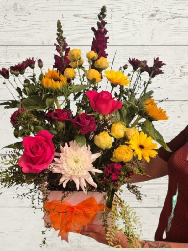 arrangement of bright flowers including yellows, reds and whites in a white box with an orange ribbon